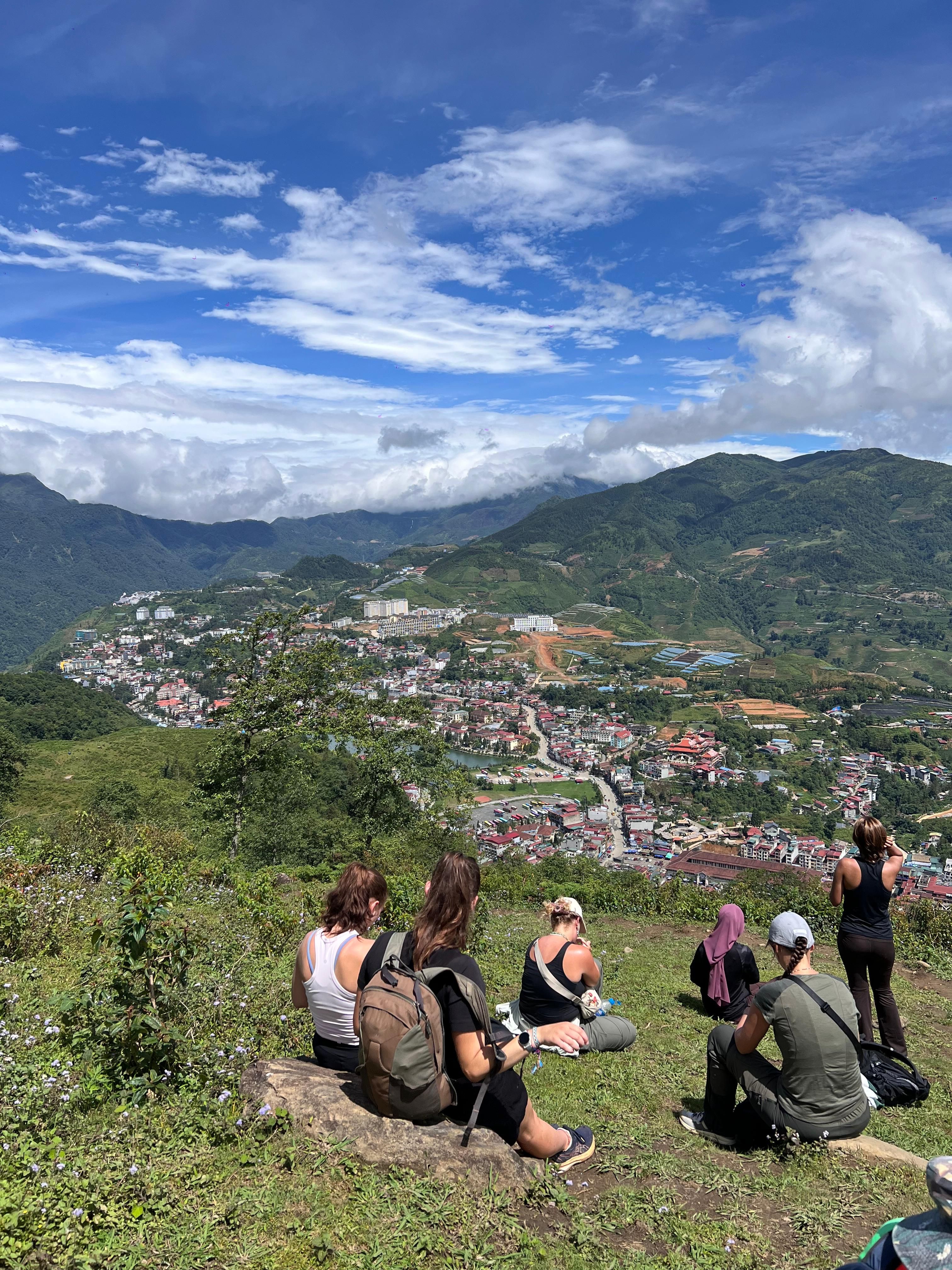 Hikers resting on a grassy hilltop above Sa Pa town and the green mountains