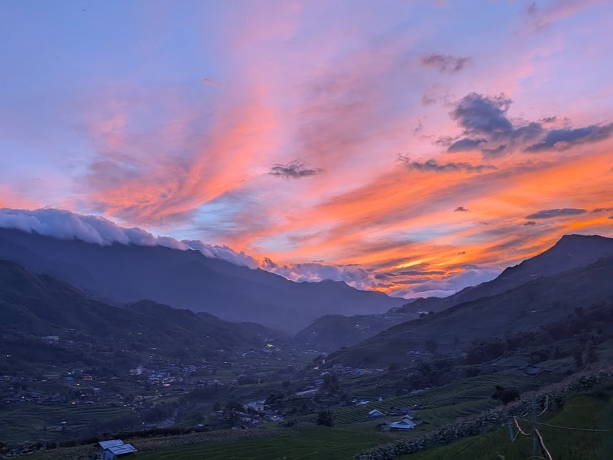 Pink and orange sunset clouds over a mountain valley and rice fields